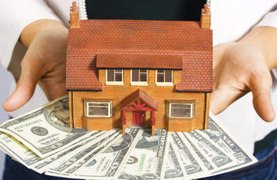 A person holding a miniature house and some dollar bills