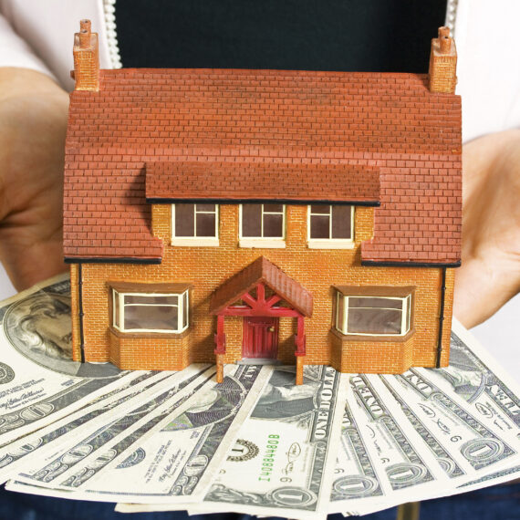 A person holding a miniature house and some dollar bills