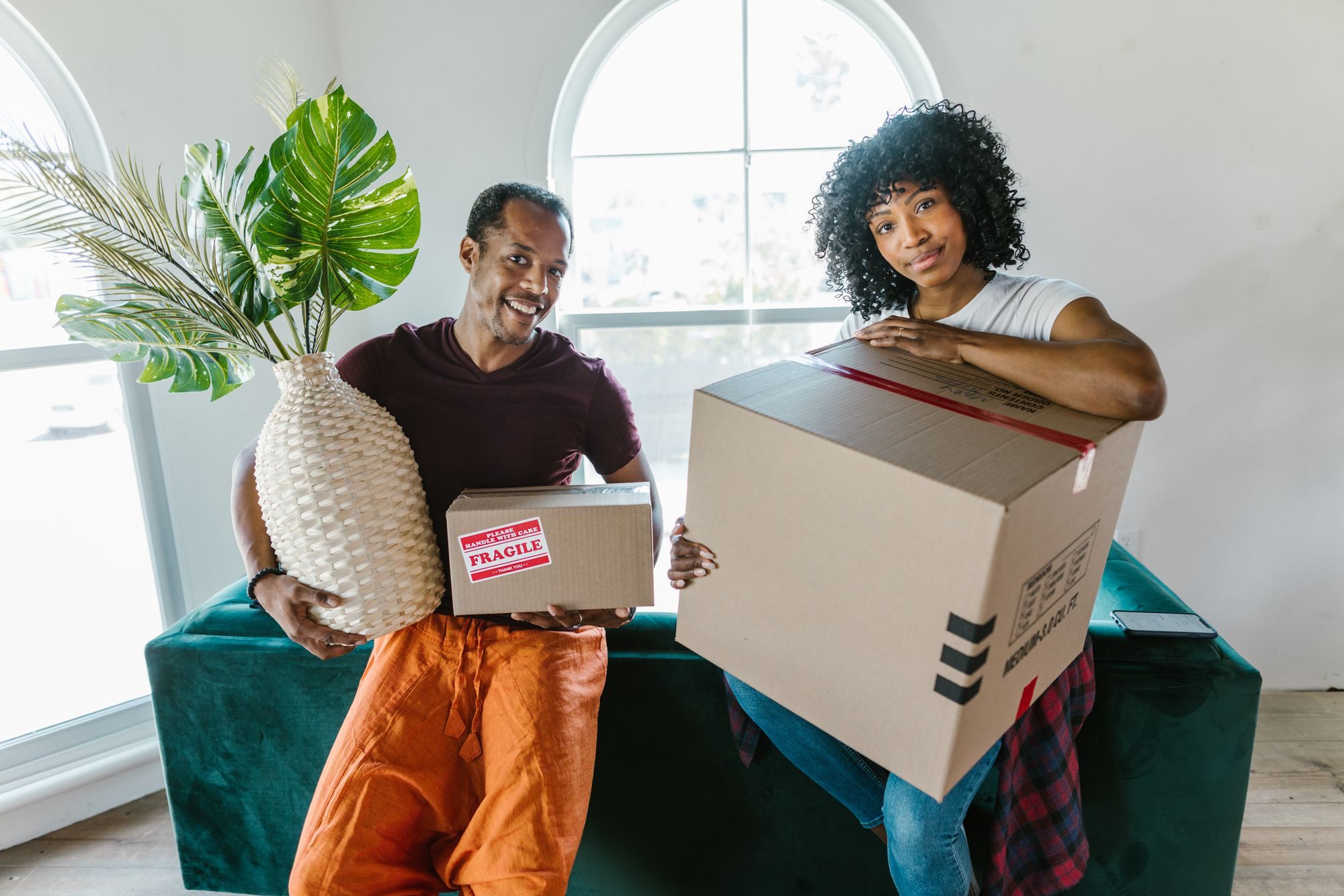Couple carrying boxes and a plant into their new home