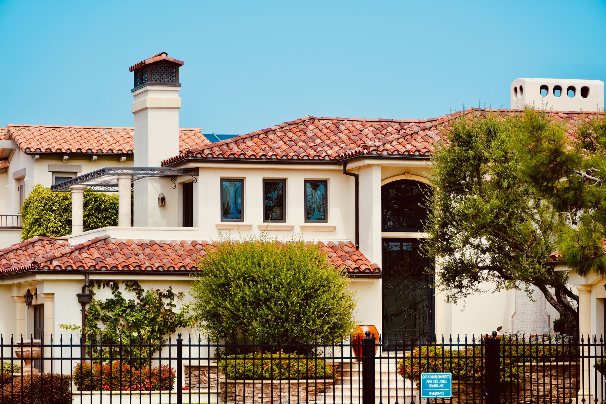 Two-story stucco home with a red tile roof and wrought-iron fence