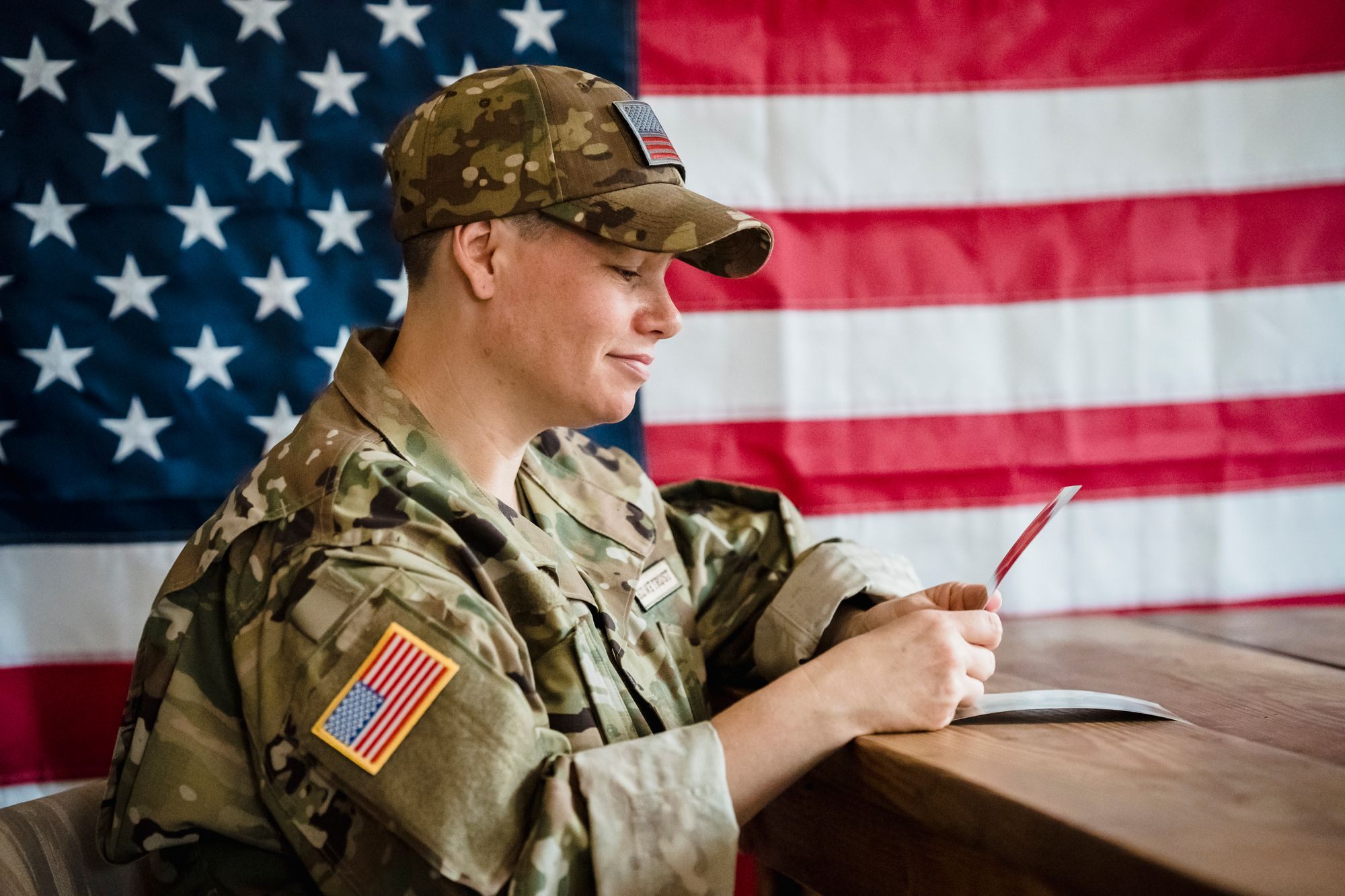 Service member in uniform at a desk with an American flag behind