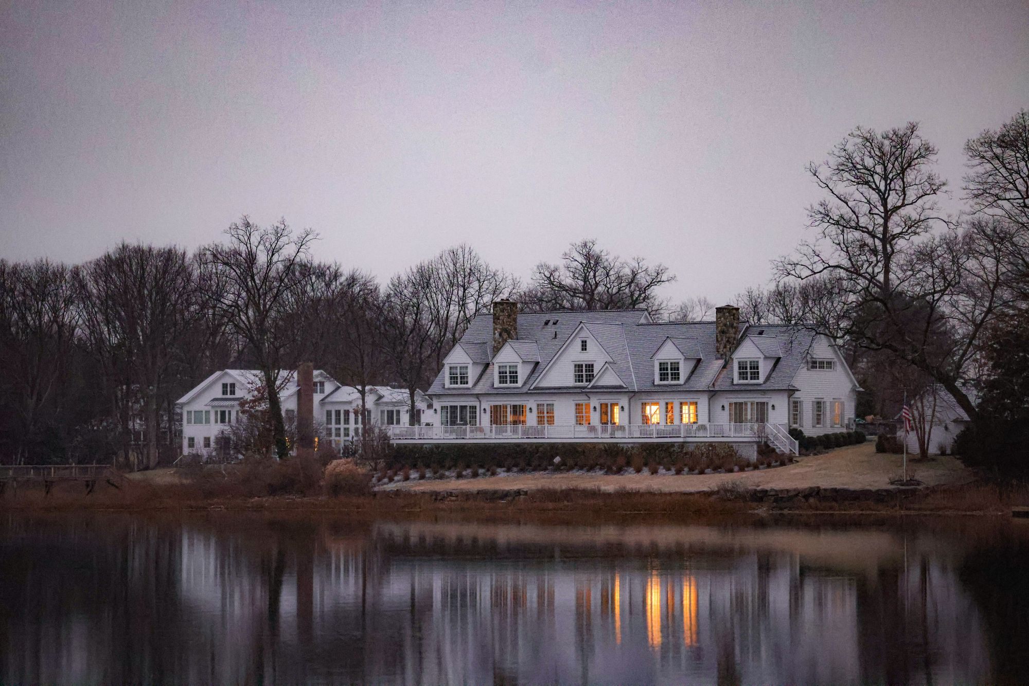 Lakefront home with lit windows reflected in the water at dusk